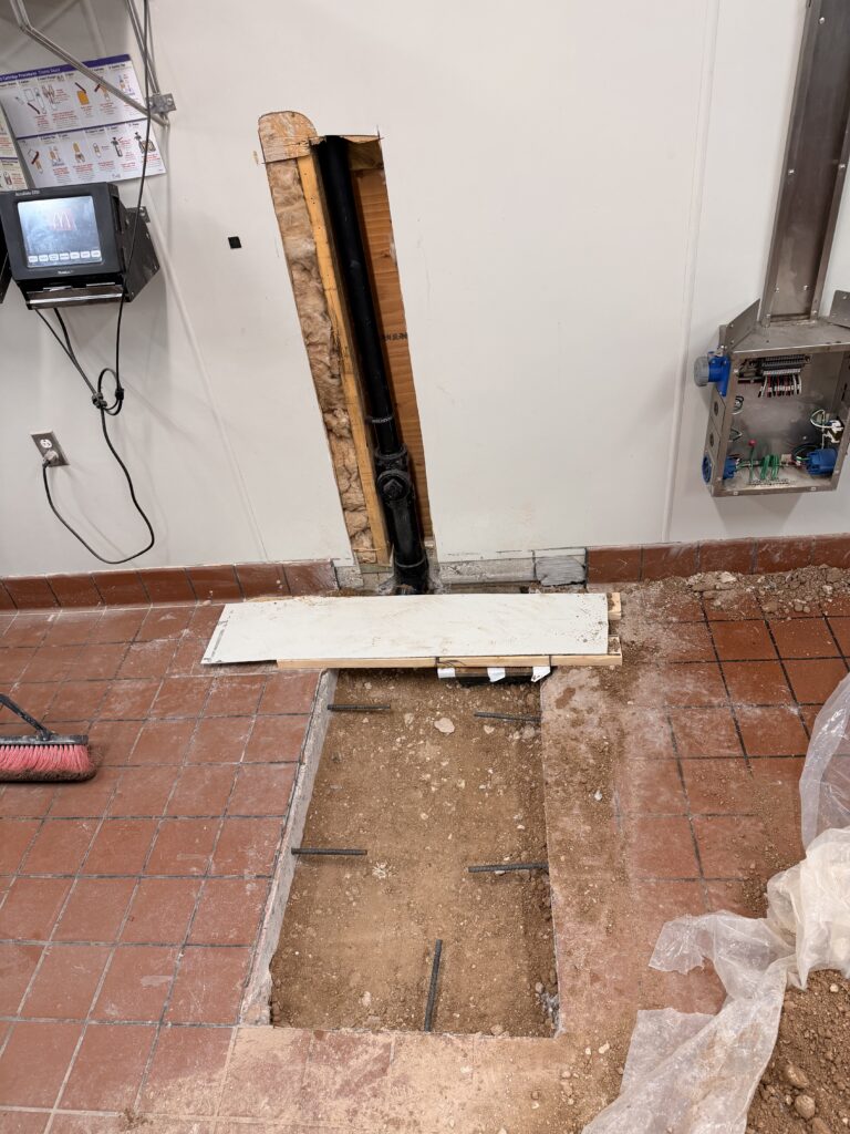 Commercial restaurant floor sink installation with piping exposed before backfill