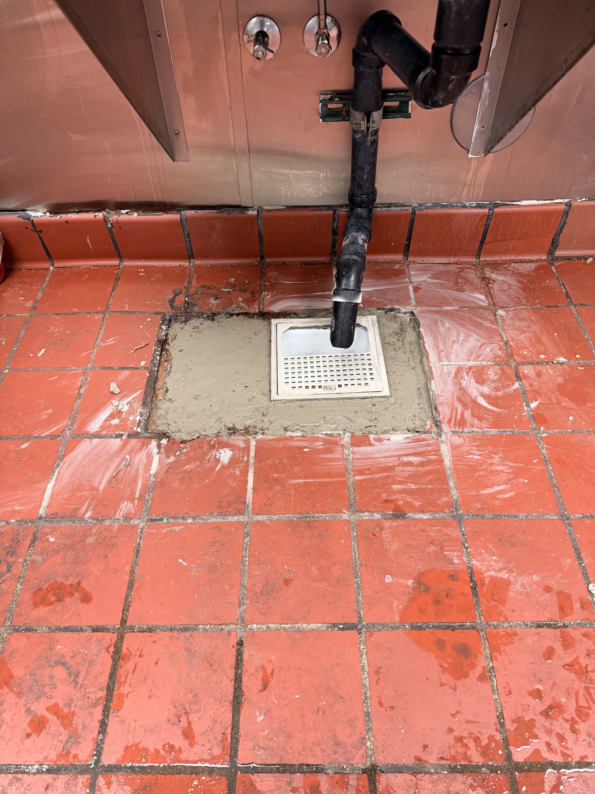 New floor sink and drainage piping installed in a restaurant kitchen with concrete floor restoration